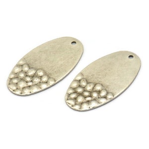 May include: Two silver oval-shaped metal charms with a textured design on the bottom half. The charms have a hole at the top for attaching to jewelry or other crafts.