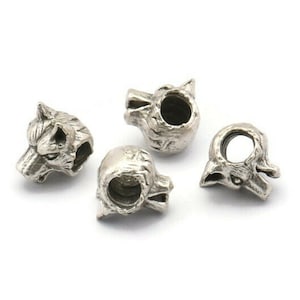 Könnte beinhalten: Vier silberne Wolfs-Kopf-Charm-Perlen. Jede Perle zeigt ein detailliertes Wolfs-Kopf-Design mit einem Loch in der Mitte zum Einfädeln.