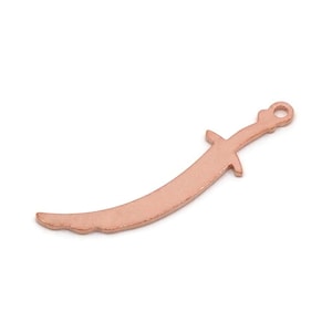 May include: A copper-colored charm in the shape of a curved sword, featuring a handle with a guard and a small loop at the top. The charm is likely for jewelry making or crafting.