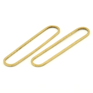 May include: Two gold-colored metal hoops, each with a slightly oval shape. The hoops are lying flat on a white surface.