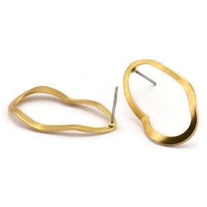 Puede incluir: Un par de pendientes de color dorado con forma ondulada asimétrica. Los pendientes están hechos de metal y tienen un cierre de poste.