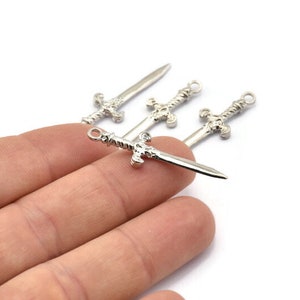 May include: Four silver sword charms with intricate details. The charms are small and delicate, perfect for adding a touch of fantasy to jewelry or crafts.