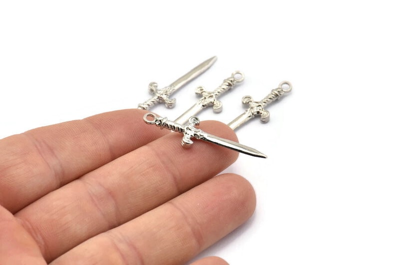 May include: Four silver sword charms with intricate details. The charms are small and delicate, perfect for adding a touch of fantasy to jewelry or crafts.