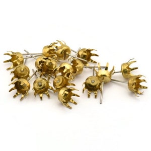 May include: A group of gold-coloured metal earring settings with a pointed end and a crown-shaped top. The settings are scattered on a white surface.