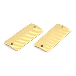 May include: Two gold-colored metal rectangular tags with a chevron pattern and two holes.