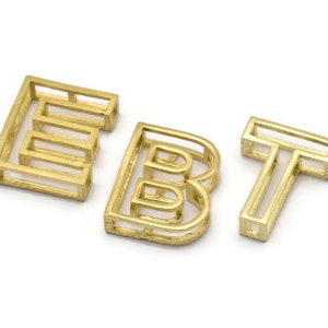 Pu&ograve; includere: Lettere in metallo dorato che compongono la parola "EBT" in uno stile moderno e geometrico. Ogni lettera &egrave; composta da pi&ugrave; quadrati sovrapposti.