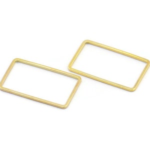 Puede incluir: Dos aros rectangulares de metal de color dorado. Los aros están abiertos y tienen un acabado liso.