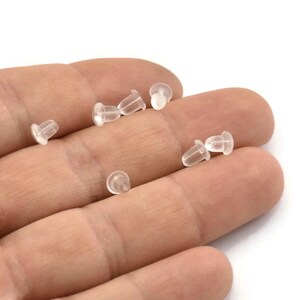 May include: A close-up of a hand holding a group of clear plastic earring backs.