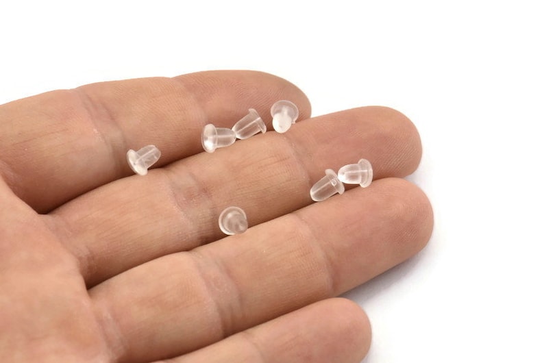May include: A close-up of a hand holding a group of clear plastic earring backs.