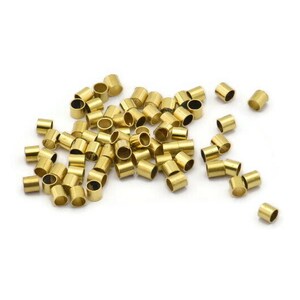 Może przedstawiać: Stosik złotych metalowych koralik&oacute;w do zaciskania, używanych do tworzenia biżuterii.