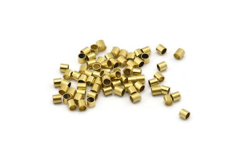 Może przedstawiać: Stosik złotych metalowych koralik&oacute;w do zaciskania, używanych do tworzenia biżuterii.