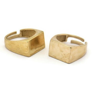 May include: Two gold-colored signet rings with square tops. The rings are simple and minimalist in design.