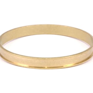 Peut inclure: Une bague en métal de couleur dorée avec une bande large et plate et un bord légèrement surélevé.