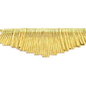 Puede incluir: Un ribete de flecos de metal dorado con una serie de finos hilos de metal texturizados. El fleco está unido a un lazo de metal en la parte superior.