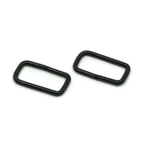May include: Two rectangular metal loops with a smooth matte black finish. Each loop features rounded corners and a visible seam where the metal ends meet, forming a continuous closed shape suitable for strap attachments or hardware components.