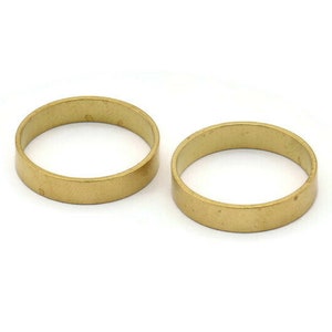 Op de afbeelding: Twee gouden metalen ringen, elk met een glad, afgerond oppervlak. De ringen zijn vergelijkbaar in grootte en vorm en liggen plat op een witte achtergrond.