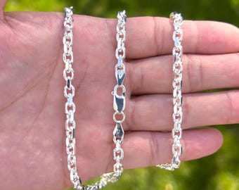 May include: A shiny silver rolo chain necklace featuring round, interlocking links and a secure lobster claw clasp. The metal surface is polished and reflective, with the word ITALY clearly stamped on the clasp mechanism.