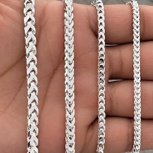 May include: Four silver-toned metal chains featuring a repeating, interlocking V-shaped link pattern. Each chain displays a polished, reflective surface with a consistent, uniform design throughout the length of the metallic links.