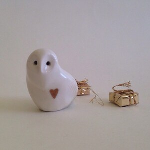 May include: White ceramic owl figurine with a small heart on its chest, next to two small gold gift boxes with gold ribbon.
