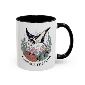 May include: White ceramic mug with a black interior and handle. The mug features a graphic of a manta ray swimming above coral and seaweed, with the words "EMBRACE THE FLOW" in navy blue.