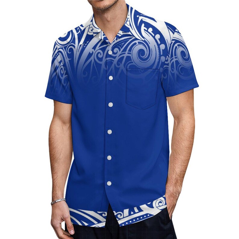 Puede incluir: Una camisa azul de manga corta con botones y un estampado tribal blanco. La camisa tiene un bolsillo en el lado izquierdo.