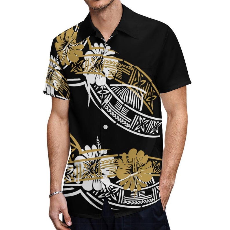 Puede incluir: Una camisa negra de manga corta con botones y un estampado polinesio blanco y dorado. La camisa presenta un patr&oacute;n floral y dise&ntilde;os geom&eacute;tricos.
