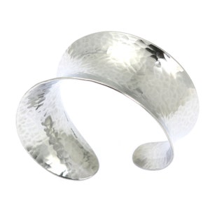 May include: A silver hammered cuff bracelet with a wide, curved design. The bracelet is made of smooth, polished metal and has a hammered texture.