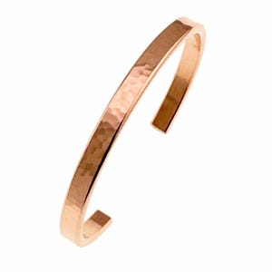 May include: A hammered copper bracelet with a smooth, polished finish. The bracelet is open and has a simple, minimalist design.