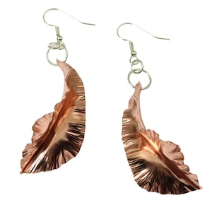 May include: A pair of rose gold earrings with a unique, ruffled petal design. The earrings are made of metal and have a silver hook closure.
