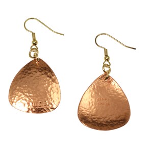 May include: A pair of hammered copper earrings with gold-tone hooks. The earrings are teardrop shaped and have a textured surface. The back of one earring has the text "USBrand Copper" stamped on it.
