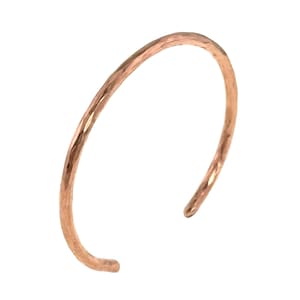 May include: A hammered copper cuff bracelet. The open-ended bracelet has a textured surface and a warm, reddish-brown color. The cuff is a simple, elegant design, suitable for everyday wear. The bracelet is approximately 2.5 inches in diameter.