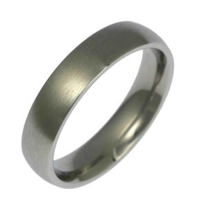 Angled close-up product image of a 5mm brushed stainless steel band ring against a plain white background. The ring features a matte brushed exterior with a soft silver tone and fine linear texture. Its edges are smoothly rounded, and the interior is polished and slightly domed for a comfort fit. Minimalist, unisex wedding band with a clean, modern design and sleek, timeless profile.