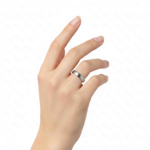 Close-up image of a woman's hand wearing a 5mm brushed stainless steel band ring on the ring finger against a plain white background. The ring features a matte silver tone with a smooth, minimalist design and softly rounded edges. The hand is slightly raised with fingers gently curved, highlighting the ring’s sleek, unisex style and clean, modern profile suitable for everyday wear or as a simple wedding band.