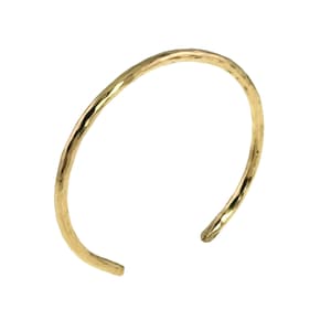 May include: A gold-colored open cuff bracelet with a hammered texture. The bracelet has a simple, elegant design and is open at the ends. The metal has a slightly irregular surface, catching the light.