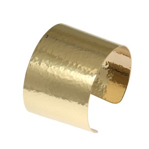 May include: A gold hammered metal cuff bracelet. The bracelet is wide and has a rounded shape.