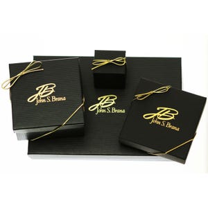 May include: Three black gift boxes with gold ribbon and the logo "John S. Brana" in gold lettering.