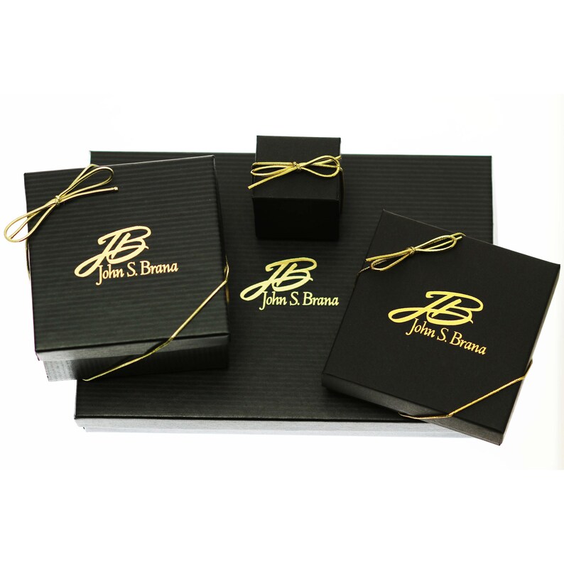 May include: Three black gift boxes with gold ribbon and the logo "John S. Brana" in gold lettering.