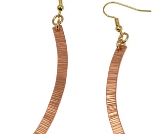 May include: A pair of copper earrings with a textured finish and gold hooks. The earrings are curved and hang down from the hooks.