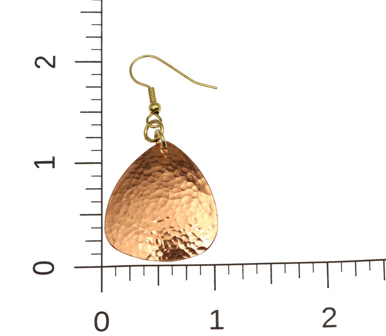 May include: A pair of hammered copper earrings with a teardrop shape and gold-tone hooks. The earrings are approximately 1 inch in length.