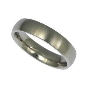 Angled product image of a 5mm brushed stainless steel band ring displayed against a plain white background. The ring features a matte brushed exterior with a soft silver tone and visible fine grain texture. The edges are gently rounded, and the interior is polished and slightly domed for a comfort fit. Minimalist unisex wedding band with a clean, modern, and timeless design.