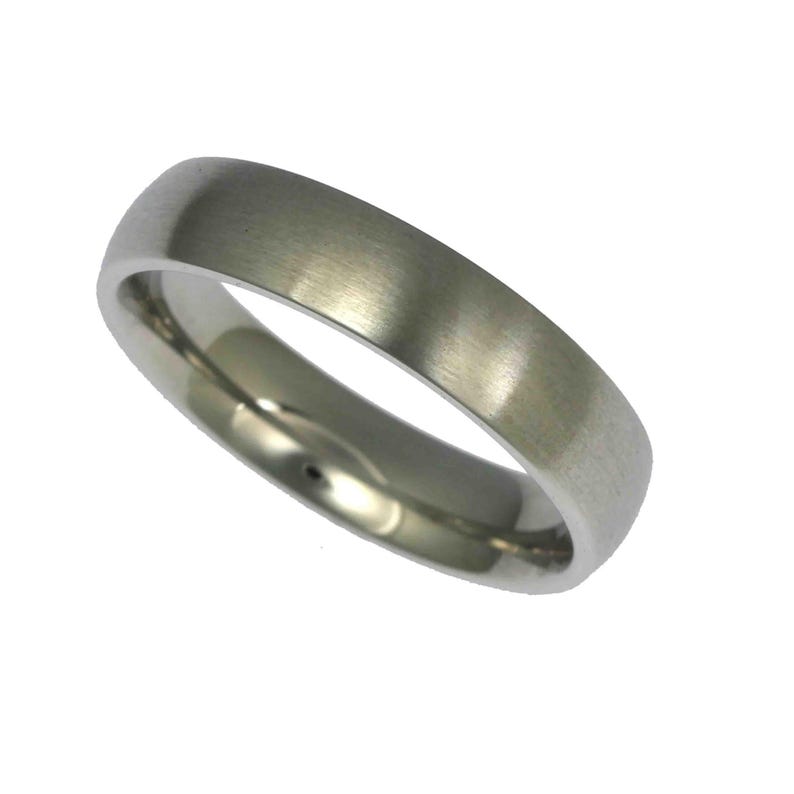 Angled product image of a 5mm brushed stainless steel band ring displayed against a plain white background. The ring features a matte brushed exterior with a soft silver tone and visible fine grain texture. The edges are gently rounded, and the interior is polished and slightly domed for a comfort fit. Minimalist unisex wedding band with a clean, modern, and timeless design.