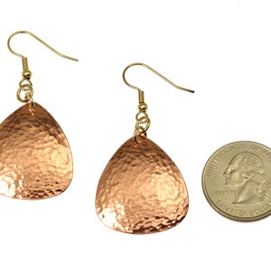 May include: A pair of hammered copper earrings with gold-tone hooks. The earrings are teardrop shaped and are about the size of a US quarter.