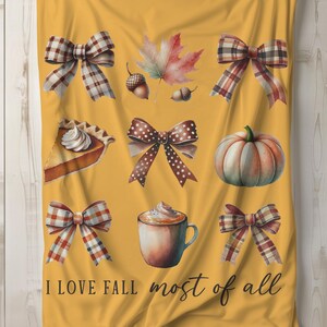 Op de afbeelding: Een gele deken met een aquarelontwerp met herfstthema's zoals pompoenen, bladeren, strikken en een kopje koffie. De tekst "Ik hou van de herfst het meest" staat op de deken gedrukt.