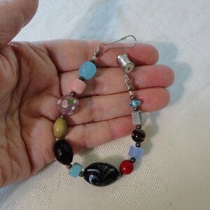 May include: A colorful beaded bracelet featuring a variety of shapes and colors. The bracelet includes beads in shades of blue, pink, black, red, and brown. The bracelet is approximately 7 inches in length.