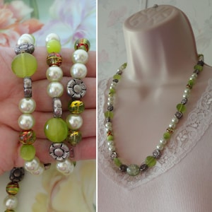 May include: A set of beaded jewelry featuring a bracelet and a necklace. The bracelet has green, white, and silver beads. The necklace has similar beads, including green, clear, and silver accents. The jewelry is displayed on a hand and a mannequin.