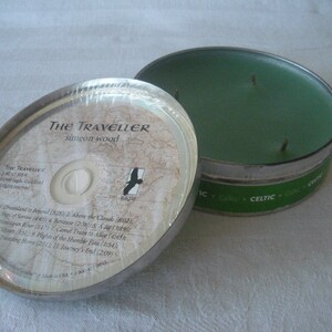 May include: An open, silver-colored tin candle with a green wax interior. The lid, with the text "The Traveller" and a map design, is partially removed. The candle is labeled "Celtic". The lid also lists song titles.