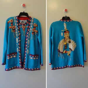 May include: A turquoise cardigan sweater with detailed embroidery and embellishments. The front features decorative elements and pockets, while the back displays a Native American figure. The sweater has red and white trim.