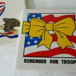 May include: A white square tile with a yellow bow over an American flag design. The text "REMEMBER OUR TROOPS" is below the flag. Another tile shows an eagle and red, white, and blue ribbons.