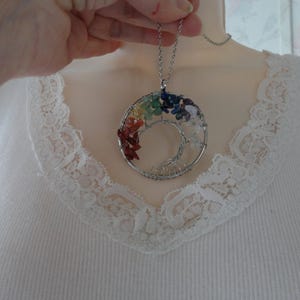 May include: A silver-toned pendant necklace featuring a spiral tree design. The spiral is adorned with colorful gemstones in a rainbow pattern. The necklace is suspended from a delicate chain, creating a unique and eye-catching accessory.