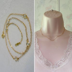 May include: A gold chain necklace featuring evenly spaced, round, clear bezel-set stones. The necklace has a delicate link design and a secure clasp. It is shown both laid out in a circular pattern and displayed on a mannequin neck form.
